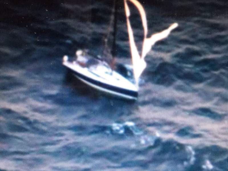 A small sailboat lit up by searchlight in heavy seas at night, mid rescue