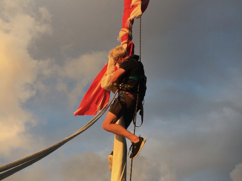 A crew member up the mast at sunset, cutting away a wrapped spinnaker
